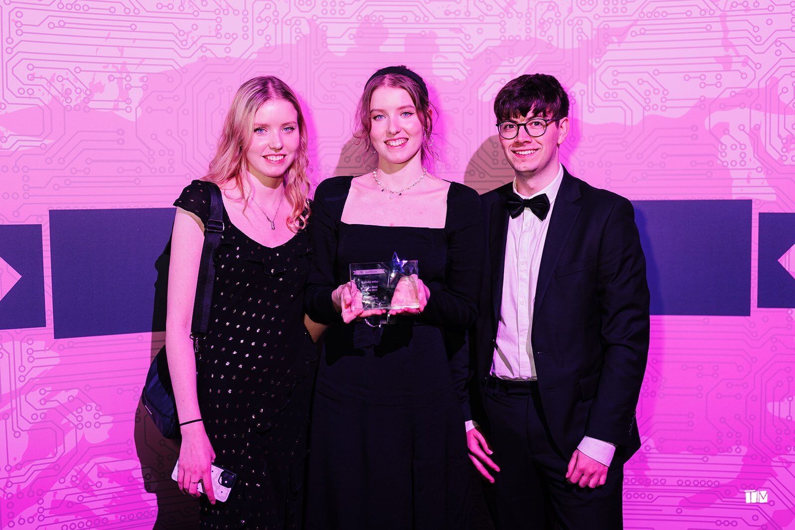 Three DevelopHER Awards winners holding their trophy in front of the pink award backdrop