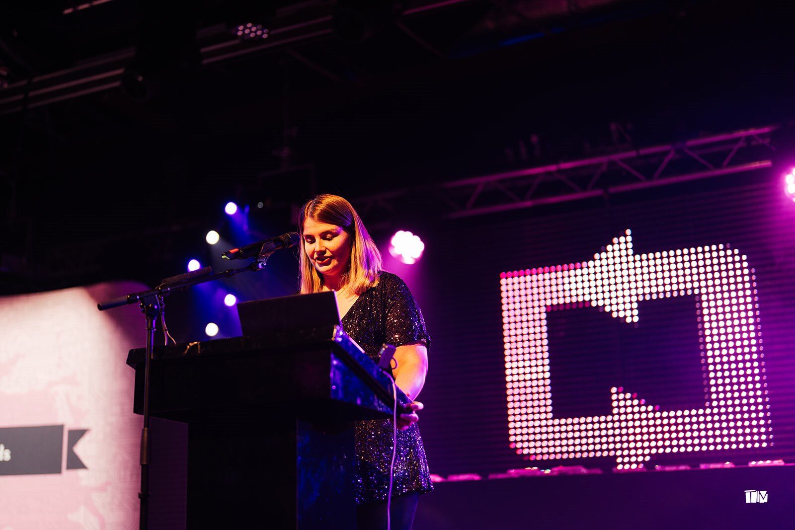 The host speaking at the lectern on stage at the DevelopHER Awards