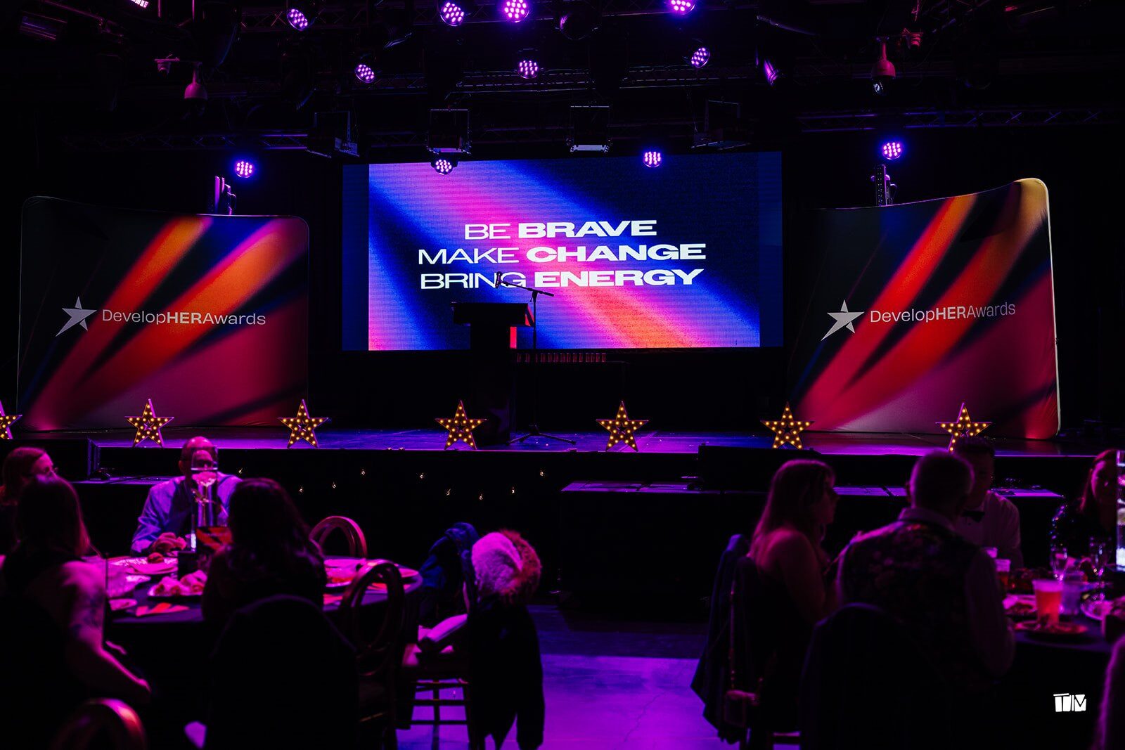 The DevelopHER Awards stage with screens reading "Be brave, make change, bring energy"